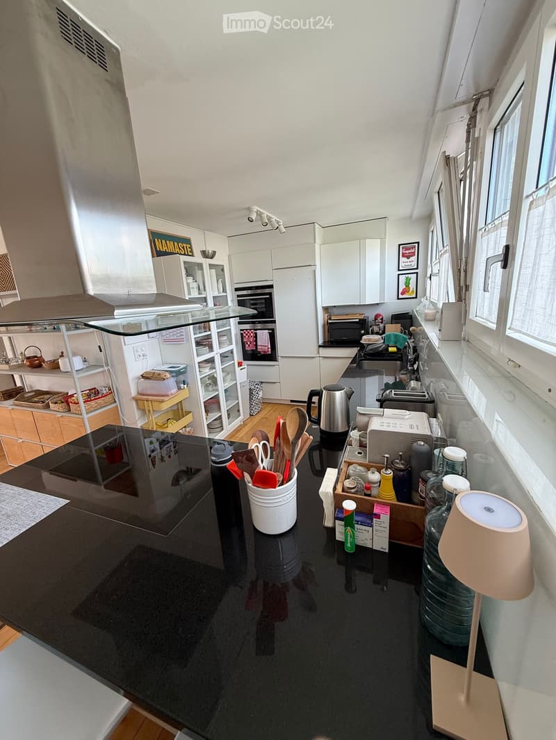 Modern kitchen with white cabinets, black countertops, and various appliances including an oven, microwave, toaster, and refrigerator. The kitchen features a central island with a black countertop, a sink, and a faucet. There are also various kitchen uten