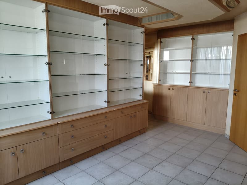 Empty room with wooden display cabinets and glass shelves, tiled floor, and wooden door frame.