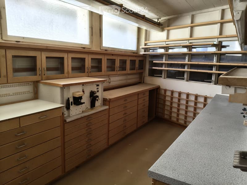 Well-lit workshop with wooden cabinets, drawers, and a countertop, featuring built-in shelves and a large window.