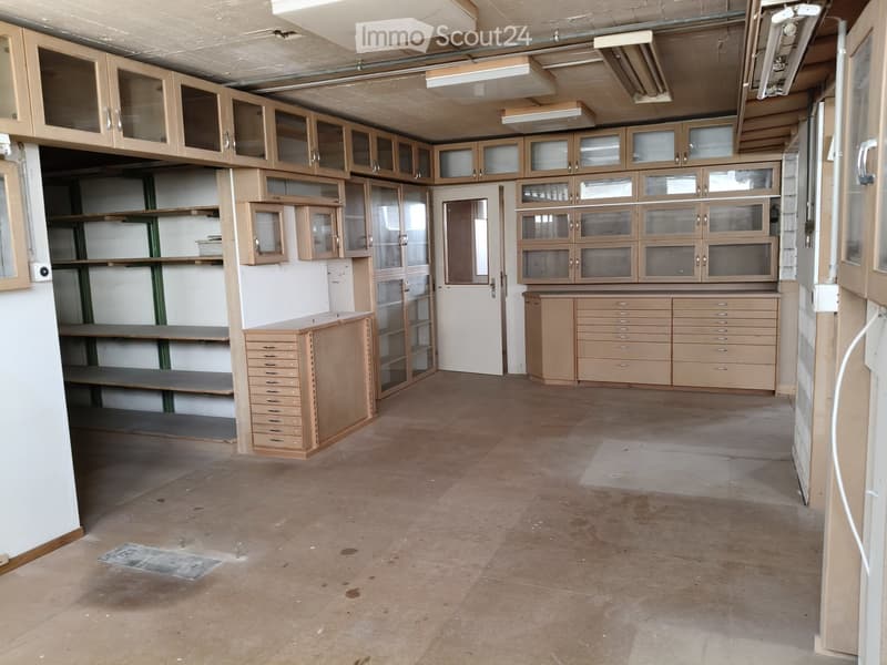 Empty room with wooden cabinets, shelves, and drawers, featuring a concrete floor and exposed ceiling pipes.