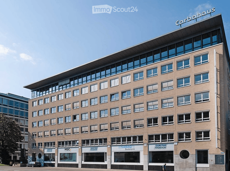 Modern multi-story building with a flat roof and large windows, featuring commercial signage for 'Carbahaus' and other businesses.