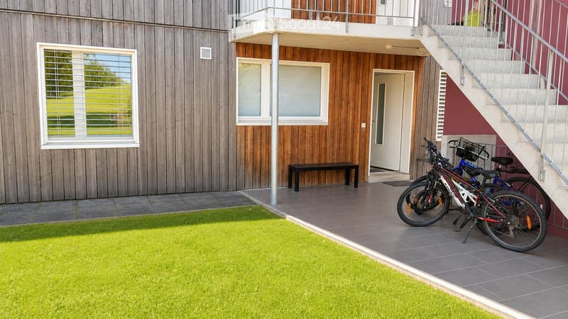 Modern two-story building with wooden facade, large windows, and a small balcony area with bicycles parked nearby.