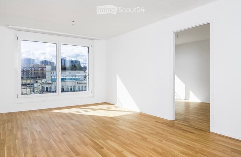 Empty room with white walls, wooden floor, large window with city view, and an open doorway leading to another space.