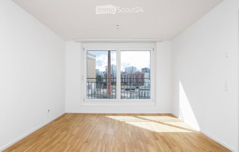 Empty room with wooden flooring, white walls, and large window with balcony view.