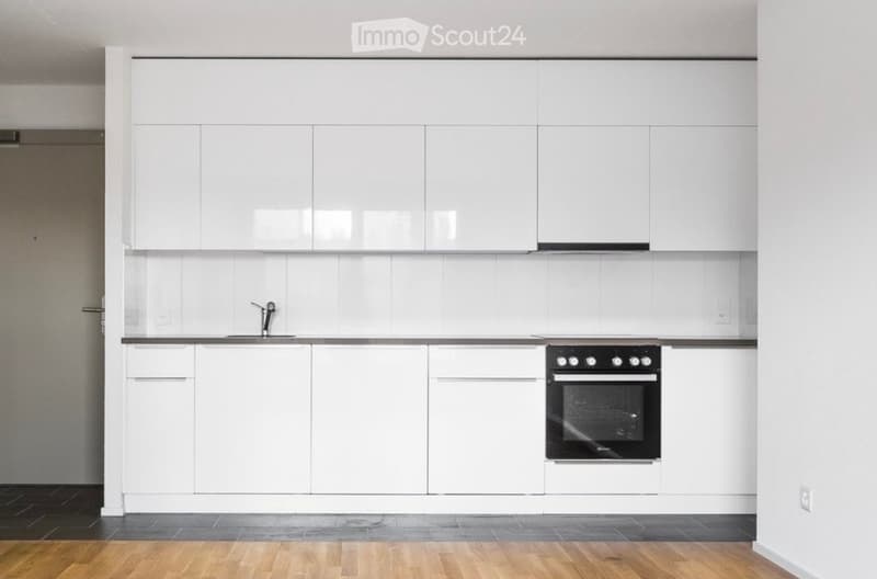 Modern kitchen with white cabinets, a sink, a faucet, and an oven. The space features a wooden floor and white tiled backsplash.