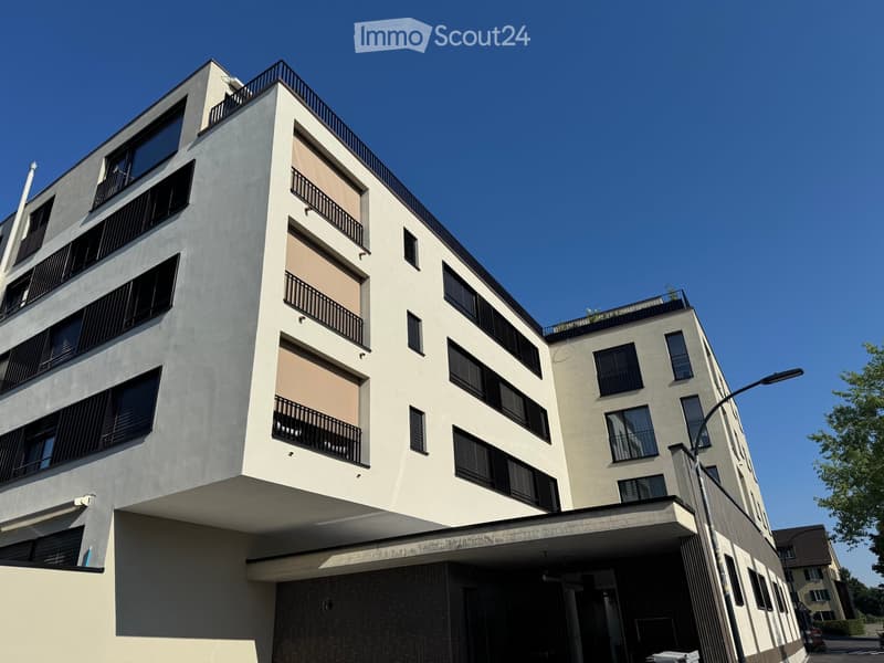 Modern multi-story residential building with balconies, large windows, and a flat roof.