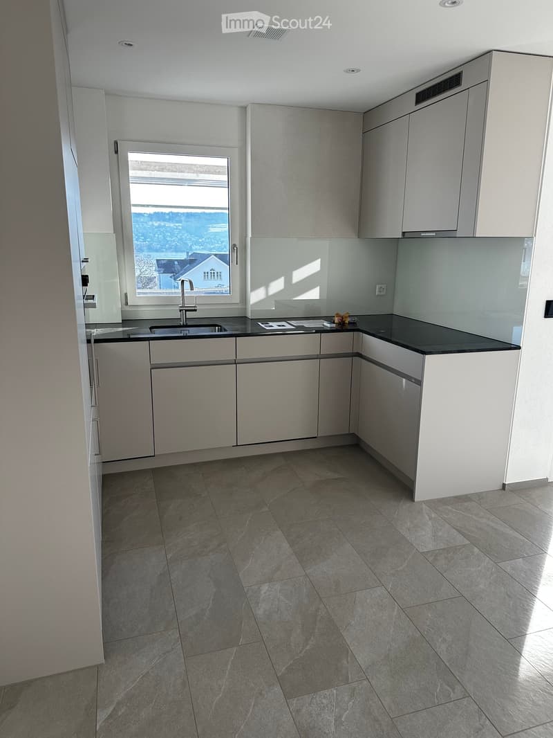Modern kitchen with grey cabinets, black countertop, and a large window offering a scenic view.