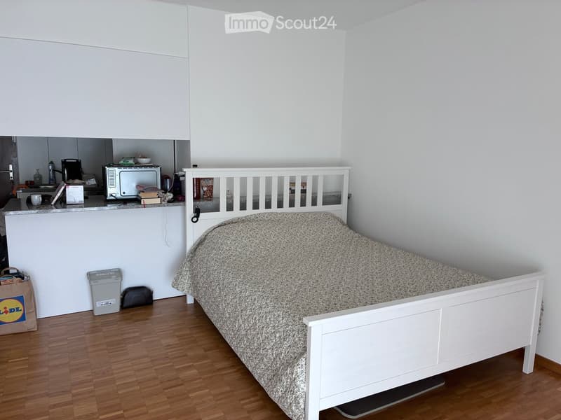 A small bedroom with a single bed, microwave, and a small kitchen area in the corner.