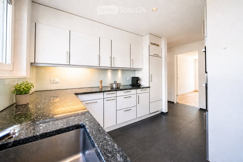 Modern kitchen with white cabinets, granite countertops, stainless steel sink, and various appliances including a coffee maker and a pot on the counter.