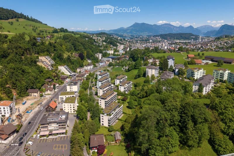 Aerial view of a town nestled in a valley with a mix of residential and commercial buildings, surrounded by green hills and mountains.