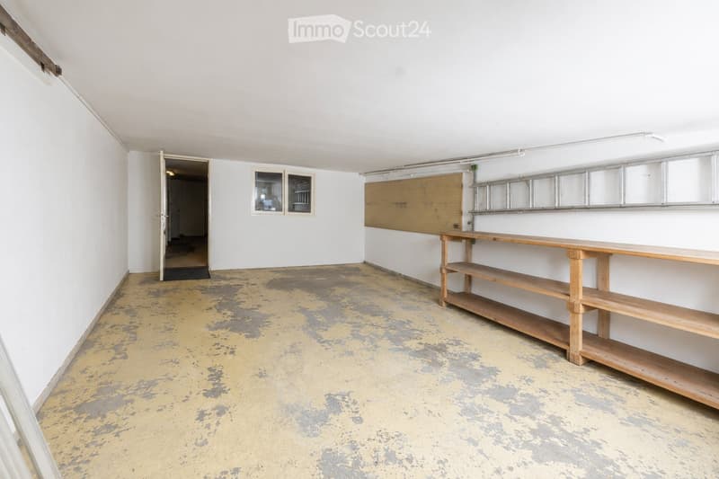 Empty room with white walls, a wooden shelf unit, and a small window. The floor is worn and discolored.