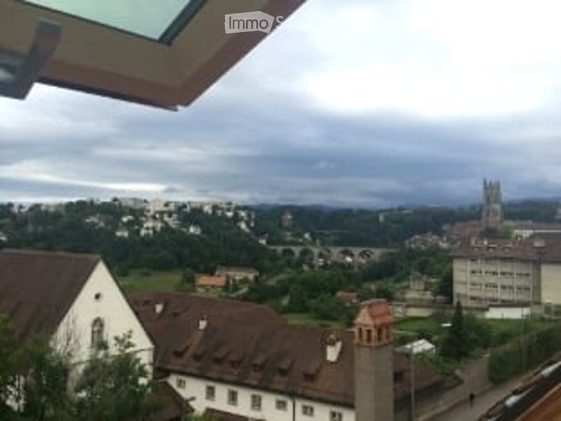 Balcony overlooking a town with visible rooftops, a church tower, and a bridge in the distance under a cloudy sky.