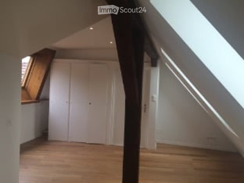 Bright, empty attic room with wooden flooring, white walls, and large skylight windows. Features built-in white closet and exposed wooden beam.