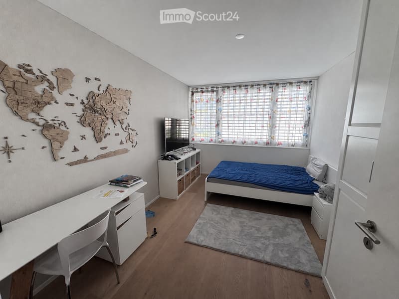 Modern bedroom with a single bed, desk, chair, shelf, and world map wall decoration. The room features wooden flooring and large windows with blinds.