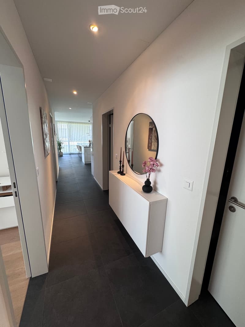 Modern hallway with dark tiled floor, white walls, recessed lighting, and a small console table with a mirror, vase, and candle holders.
