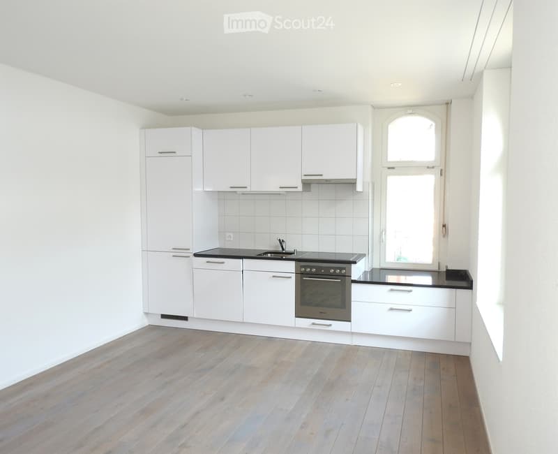 Modern kitchen with white cabinets, stainless steel appliances, and light wooden flooring.
