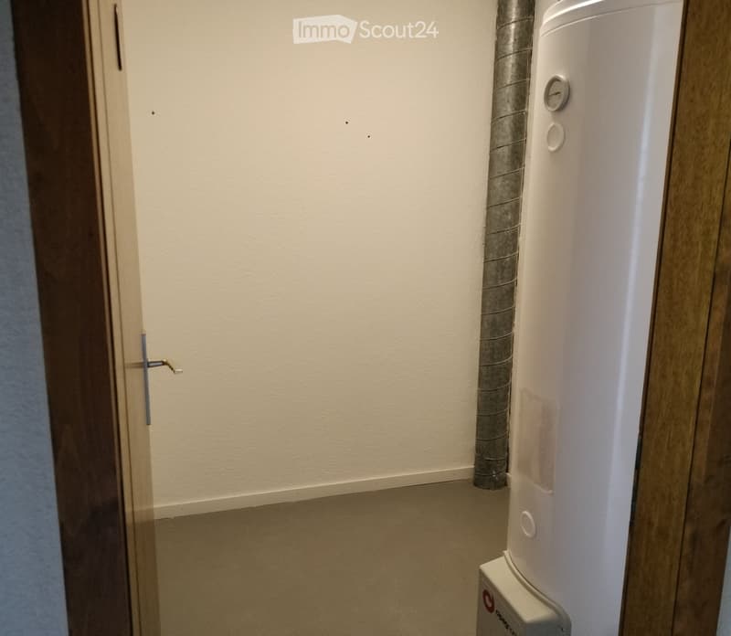 Unfurnished Room. Empty room with light-colored walls and a white appliance, likely a water heater, positioned against the wall. The door is slightly ajar, revealing a glimpse of another room.