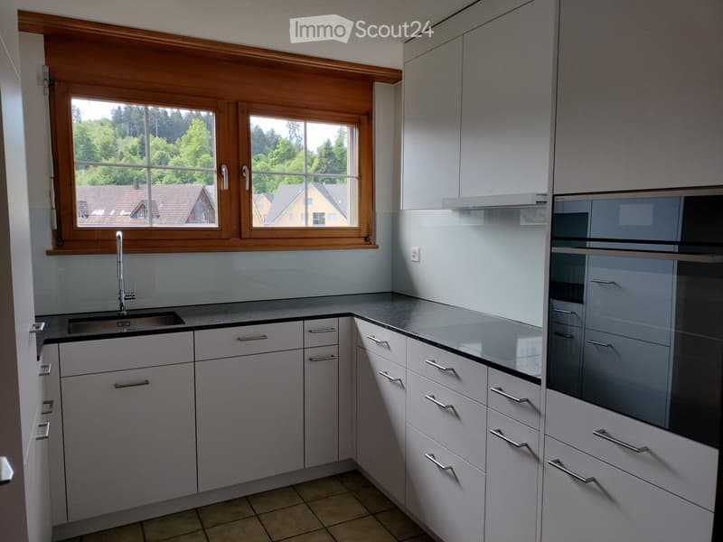 Kitchen. Modern kitchen with light grey cabinets, stainless steel appliances, and a large window overlooking a green area.