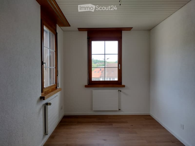 Unfurnished Room. Empty room with wooden flooring, white walls, and two windows with wooden frames. Radiators are present under each window.