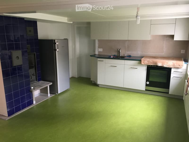 Modern kitchen with white cabinets, green flooring, stainless steel appliances, and a small bench near the wall.