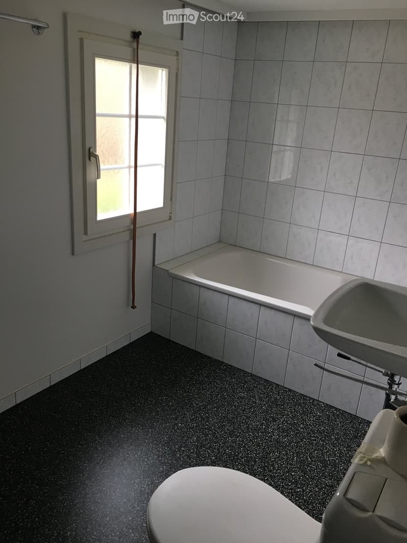 Bathroom with a bathtub, sink, and toilet, featuring tiled walls and a dark speckled floor.