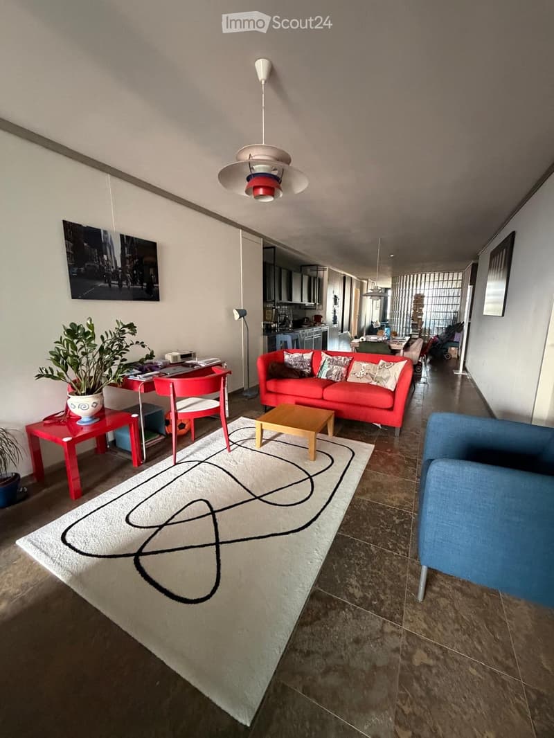 Modern living room with a red sofa, coffee table, blue armchair, red side table, potted plant, and a large abstract rug on the floor.