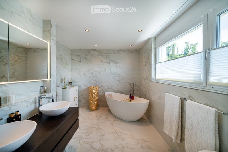 white marble tiles, two vanity sinks, freestanding bathtub, golden vase, marble wall, large window, towel racks
