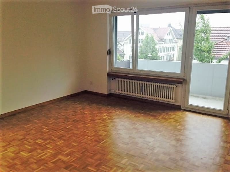 Empty room with wooden flooring, large window, radiator, and white walls.