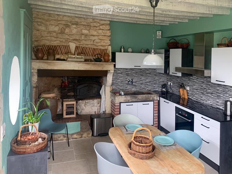 A rustic kitchen with a stone fireplace, modern cabinets, a wooden dining table, and various kitchen appliances.