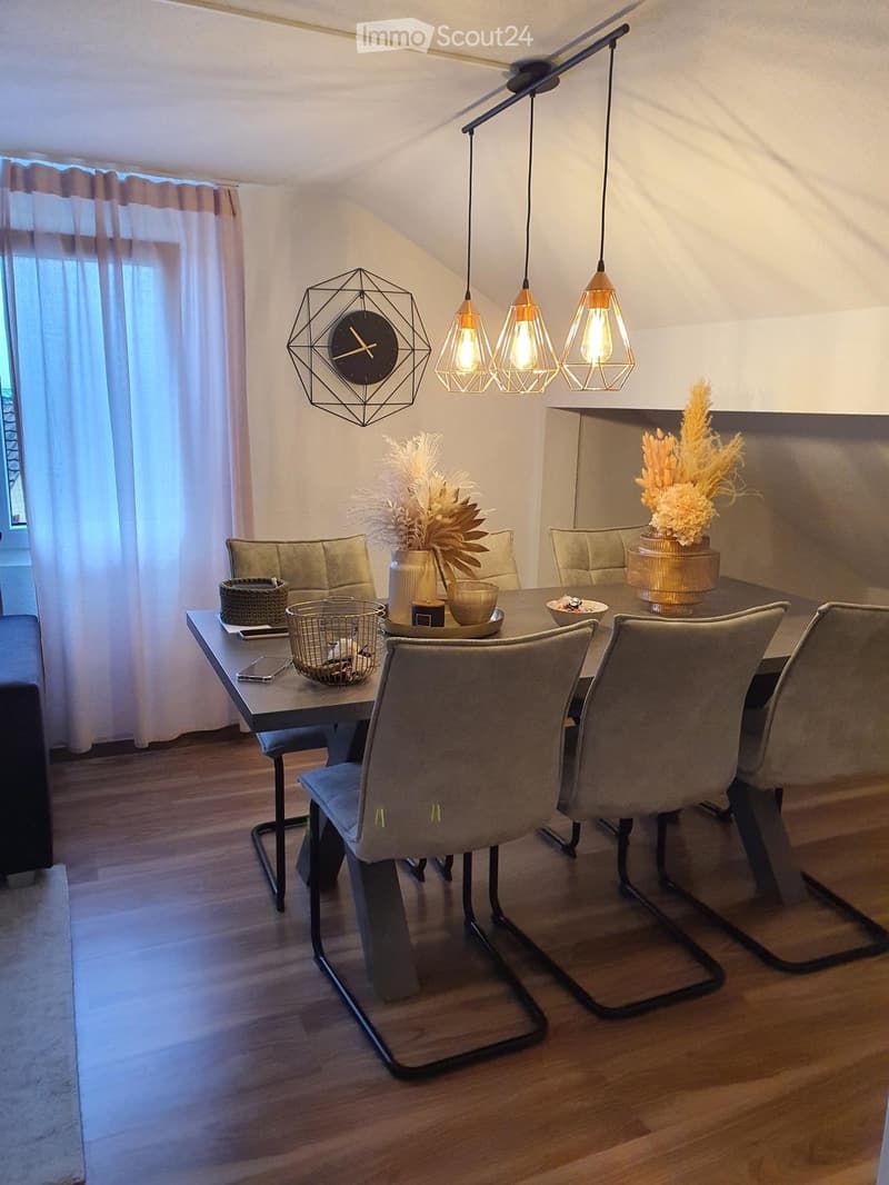 Modern dining area with a sleek table, chairs, decorative vases, a clock, and pendant lights.