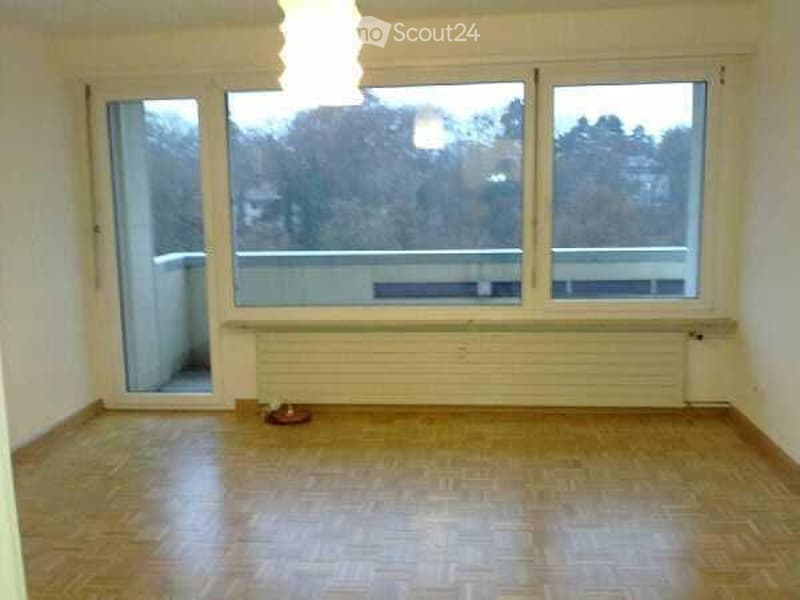 Empty room with wooden flooring, large windows, and a balcony access door. No furniture or equipment present.