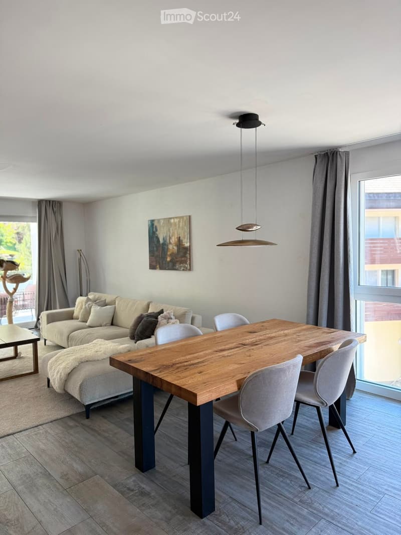 Modern living and dining area with a beige sofa, wooden dining table, grey chairs, floor lamp, and artwork on the wall.