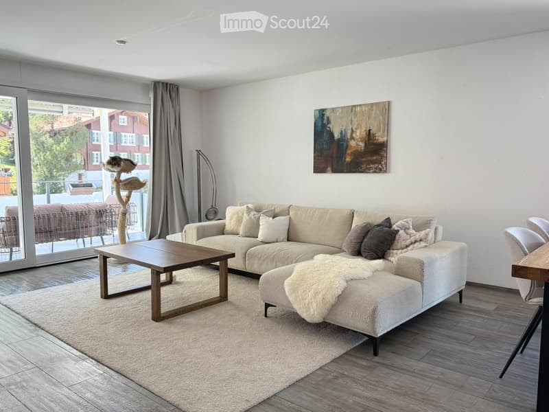 Modern living room with a large sectional sofa, coffee table, floor lamp, and a cat tree near the large window with a view of the outdoor area.
