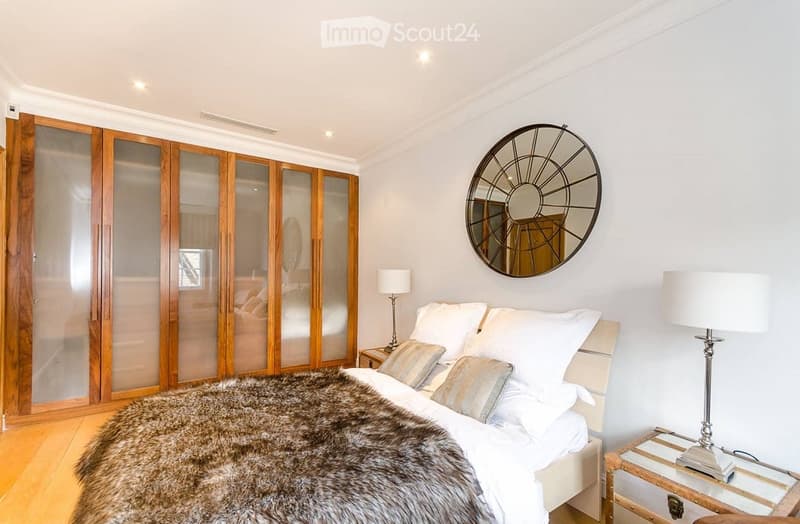 Modern bedroom with a large bed, fur throw, nightstands, lamps, and a large mirrored wardrobe.