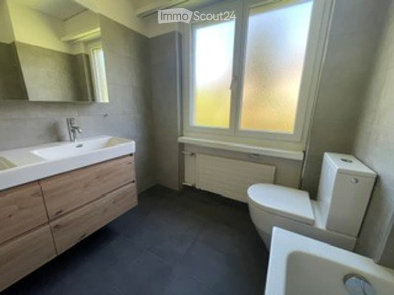 Modern bathroom with a large window, wooden vanity with sink, mirror, toilet, bathtub, and radiator.