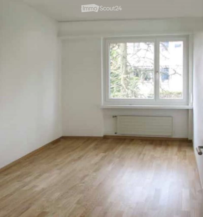 Empty room with wooden flooring, white walls, and a single window with a radiator below it.