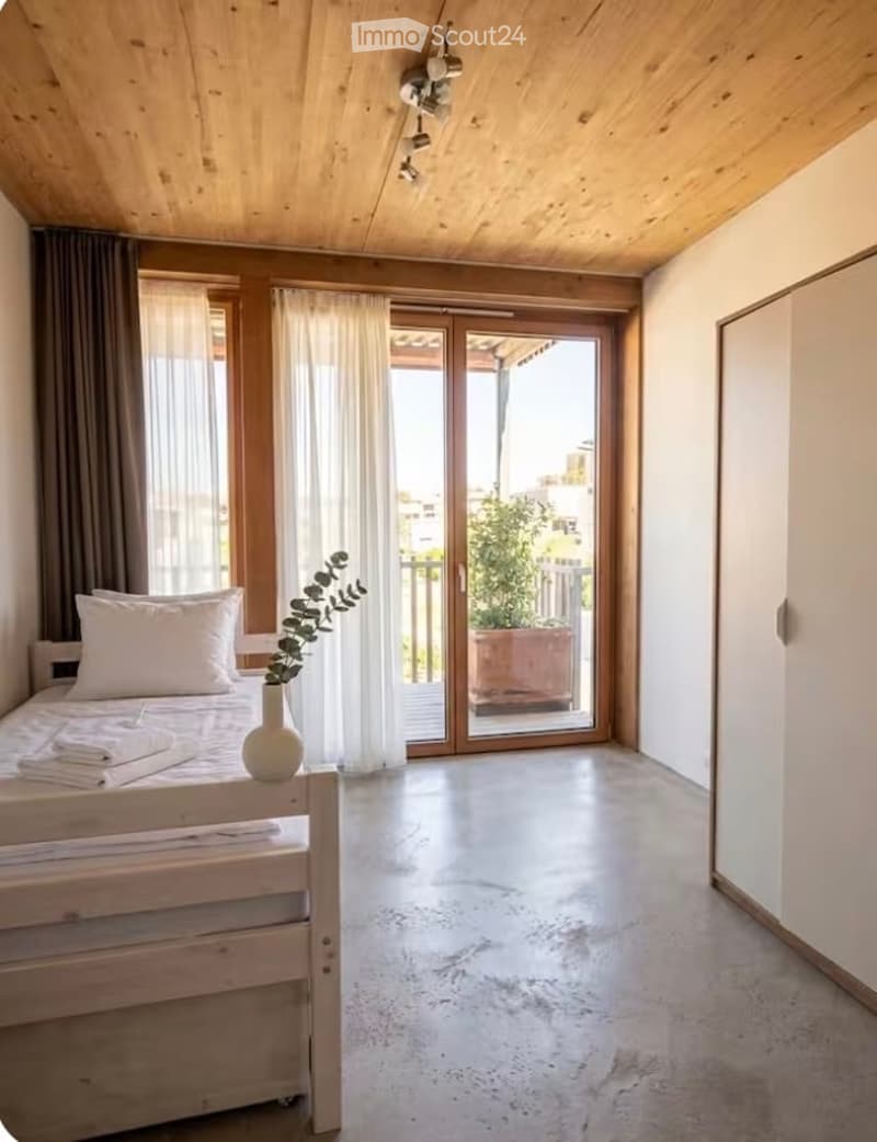 Modern bedroom with a wooden bed, white wardrobe, large windows with curtains, and a sliding glass door leading to a balcony.