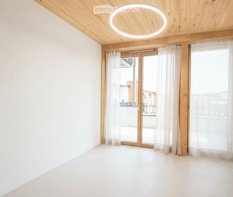 Empty room with white walls, wooden ceiling, large sliding glass doors with white curtains, and a circular ceiling light fixture.