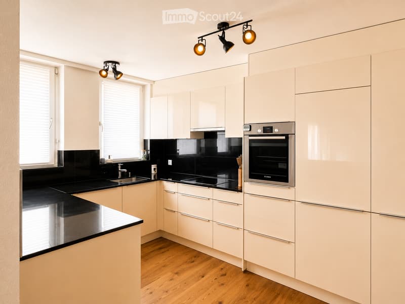 Modern kitchen with light-colored cabinets, black countertops, and stainless steel appliances, including an oven and a sink.