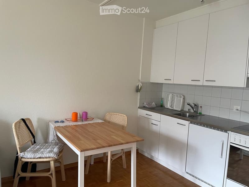 Modern kitchen with white cabinets, wooden dining table, two chairs, and a sink with a faucet.