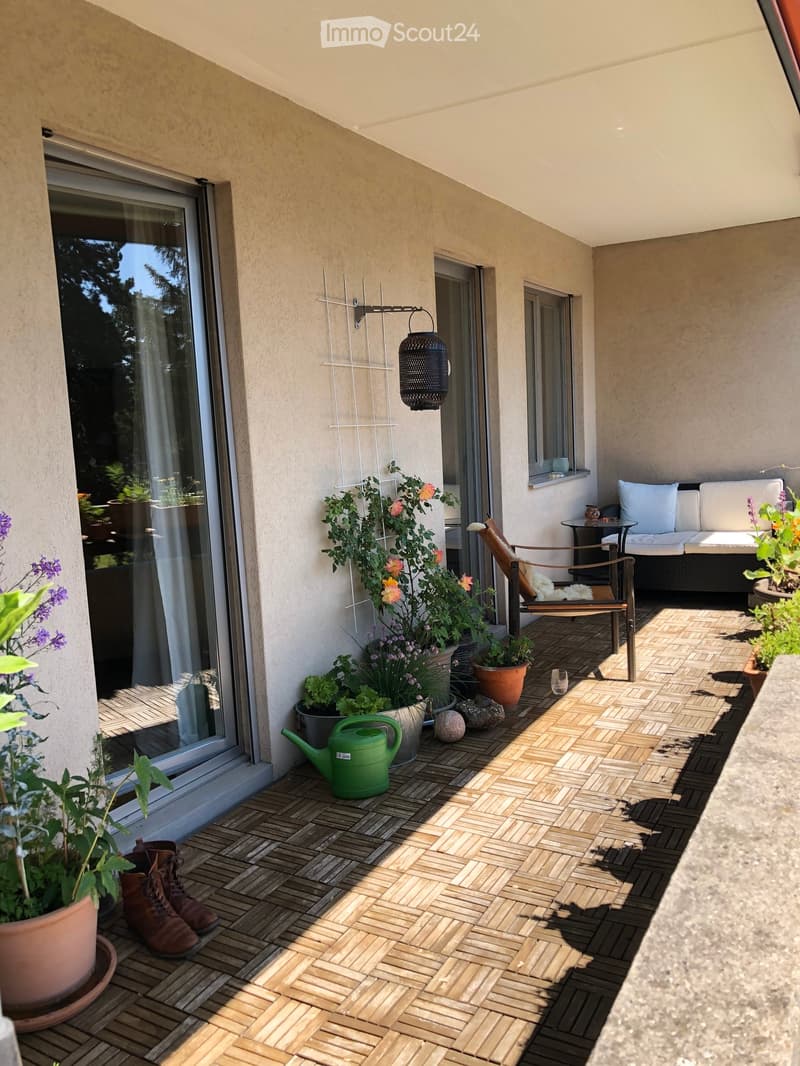 Balcony with wooden decking, potted plants, a sofa, a chair, a small table, and a green garden hose.