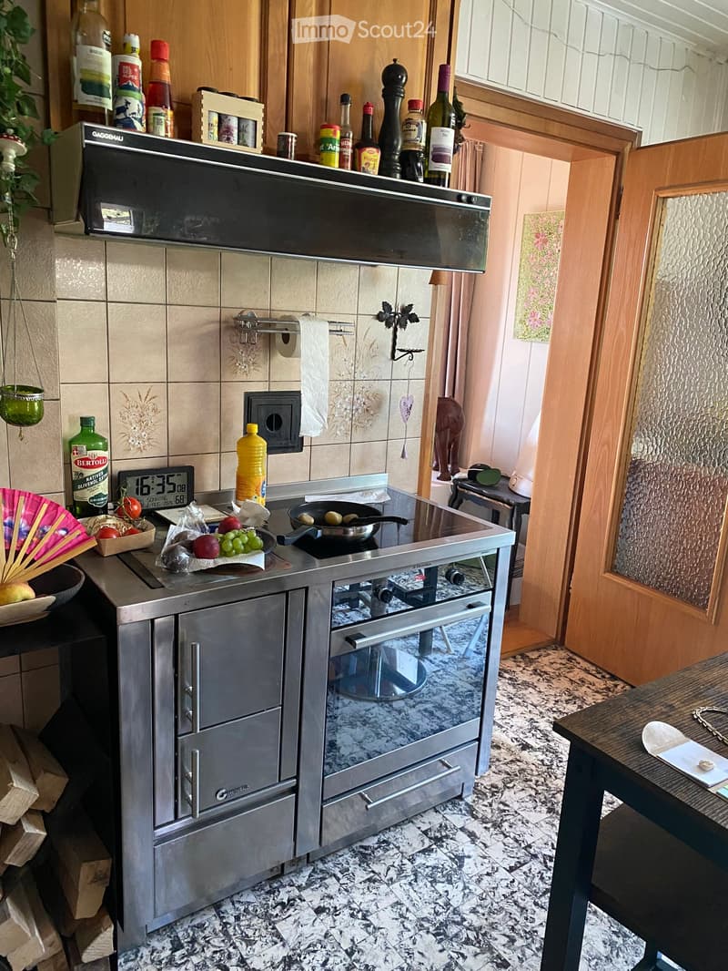 Modern kitchen with stainless steel appliances, granite countertops, and various bottles and items on the counter and shelves.