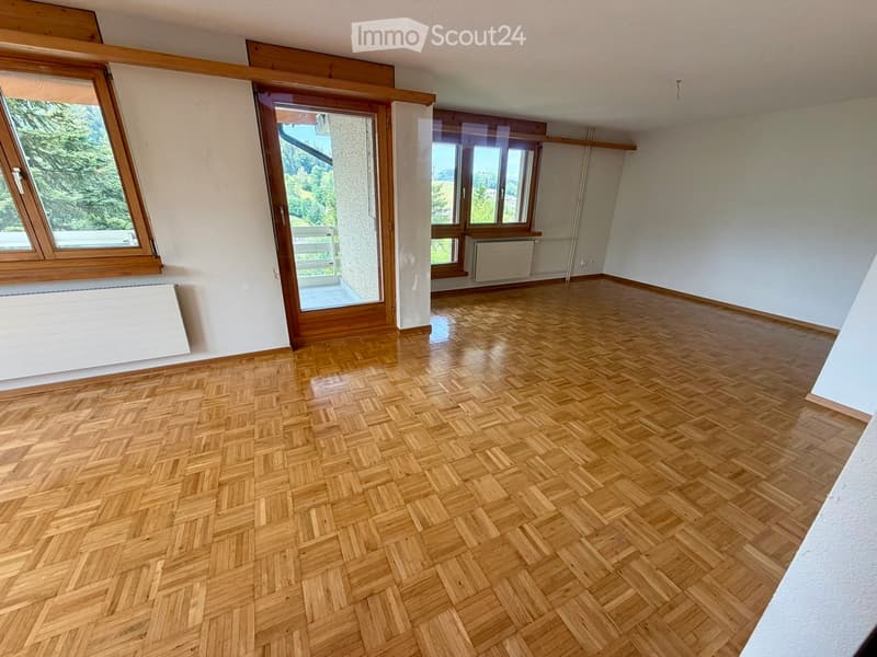 Empty room with wooden herringbone flooring, large windows, and a sliding glass door leading to a balcony.