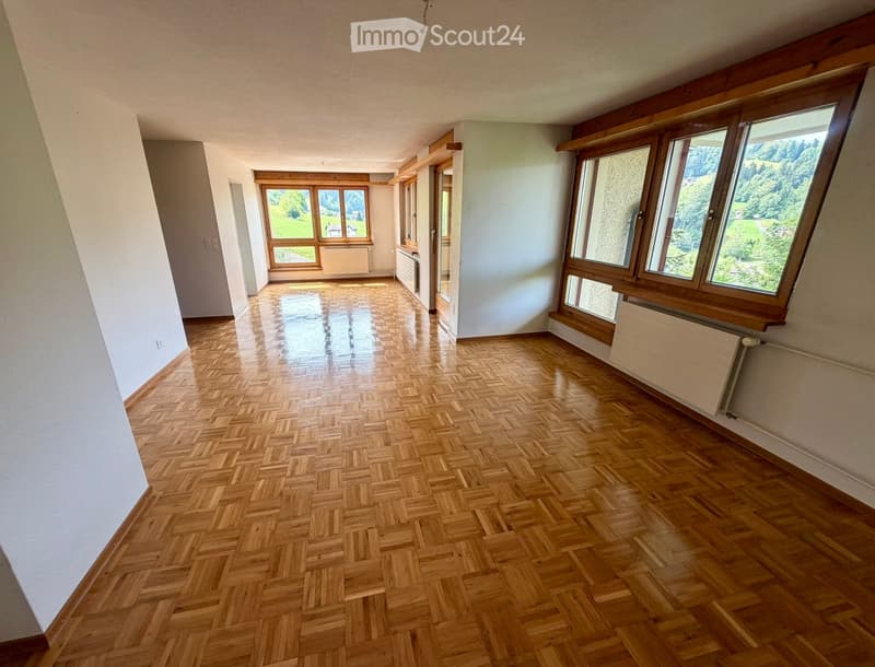 Empty room with wooden herringbone flooring, large windows with wooden frames, white walls, and radiators visible.