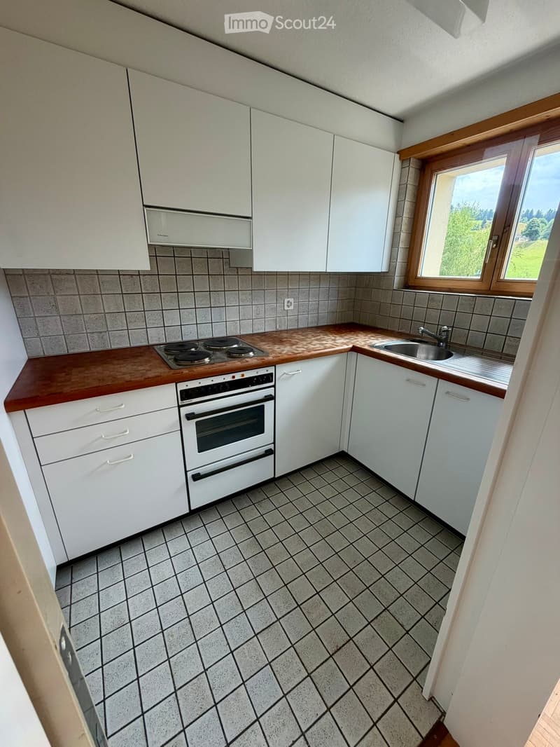 Modern kitchen with white cabinets, wooden countertops, and a tiled floor. Features an electric stovetop, oven, and sink.