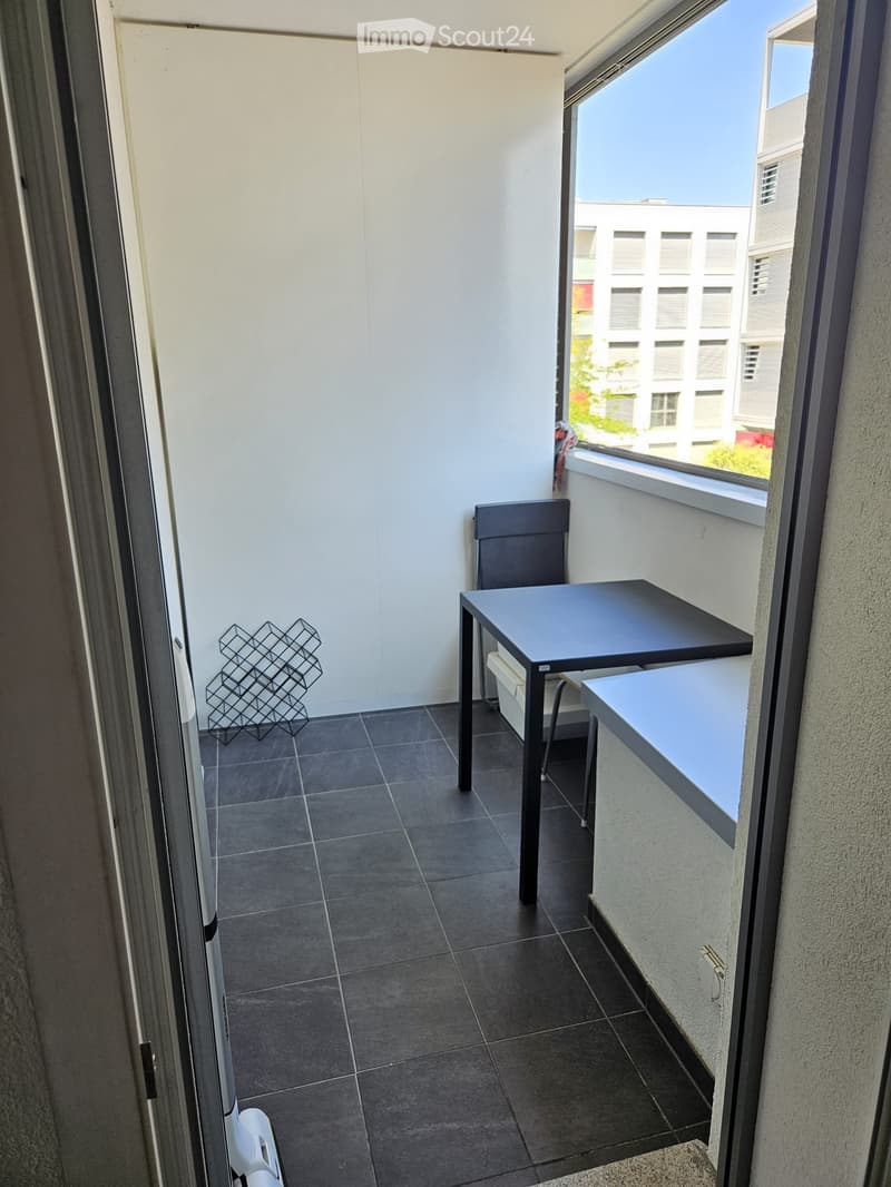 Balcony with dark tiled floor, white walls, a small black table with a chair, and a metal shelf on the left side.