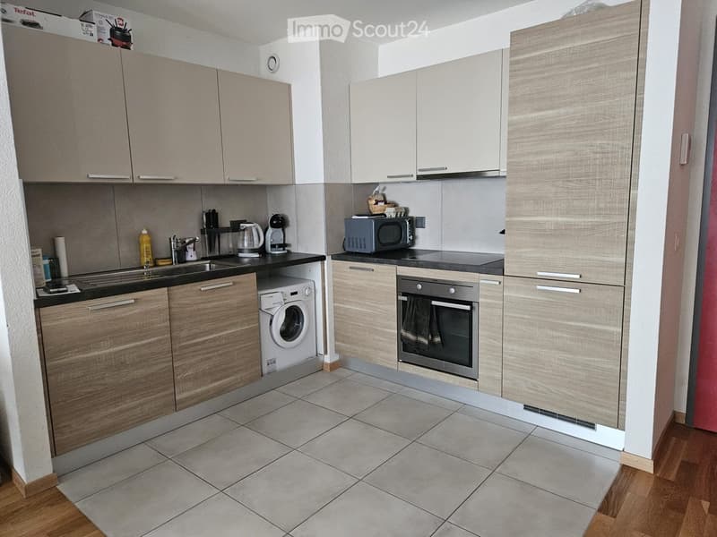 Modern kitchen with light wood cabinets, stainless steel appliances, and tiled flooring.