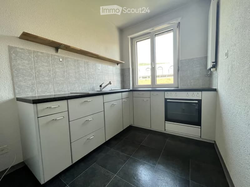 Modern kitchen with white cabinets, black countertops, and a built-in oven. Features a window above the sink and wooden shelf above the counter.