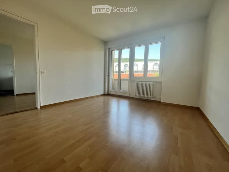 Empty room with wooden flooring, white walls, large windows, and a radiator. No furniture or equipment present.