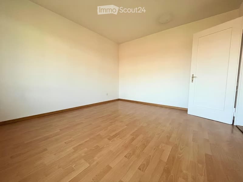 Empty room with light wooden flooring and white walls, featuring a closed white door on one side.